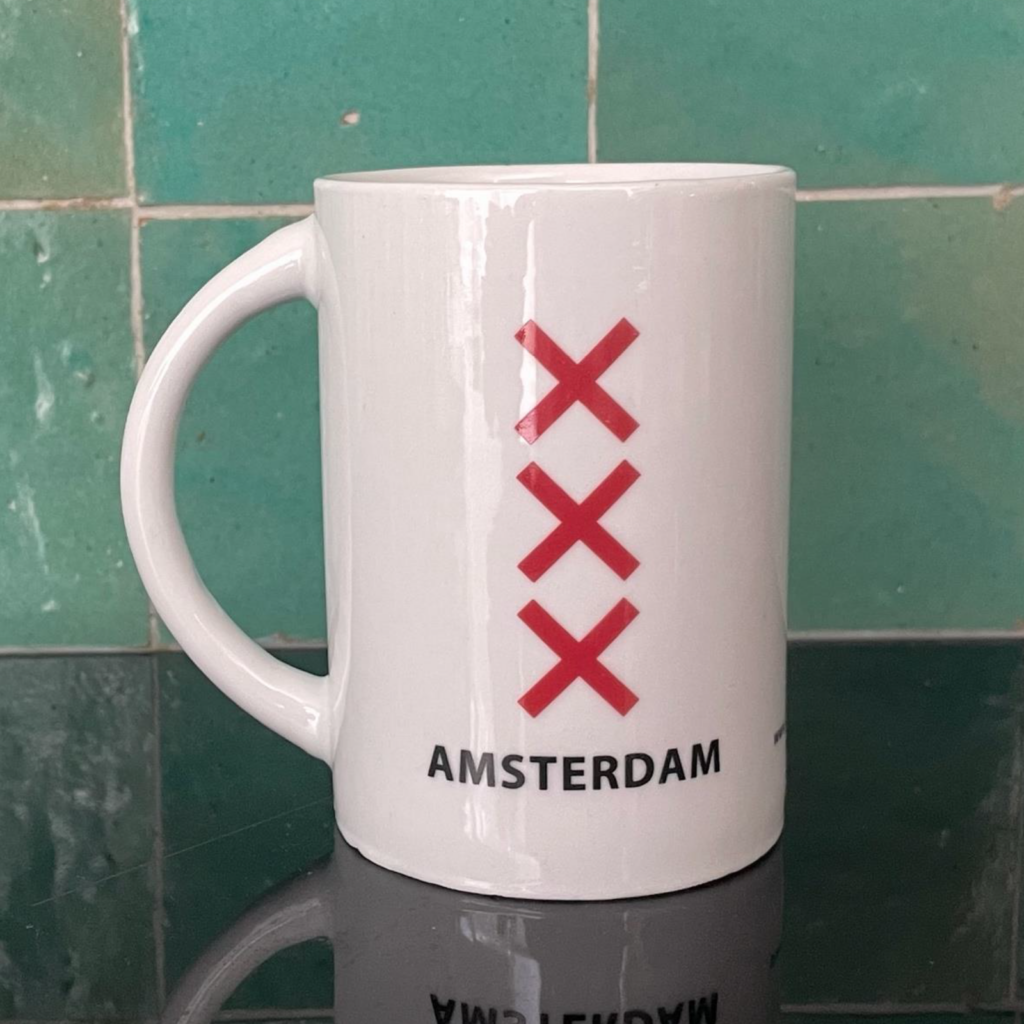 Een witte beker, aan twee kanten bedrukt, de ene kant met 'Amsterdam' en de andere 'Rotterdam'. Deze kant toont: "Amsterdam", met 3 rode kruizen (dat is het stadslogo, ook wel bekend de 3 Andreaskruisen.